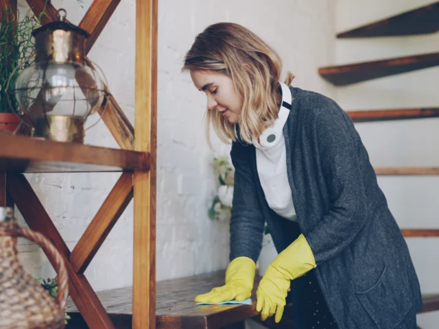 Cleaner in yellow gloves wiping down a wooden sideboard