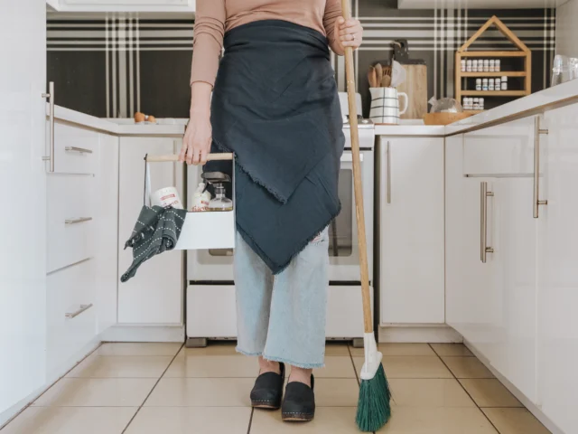 Cleaner with a broom in an empty rental kitchen