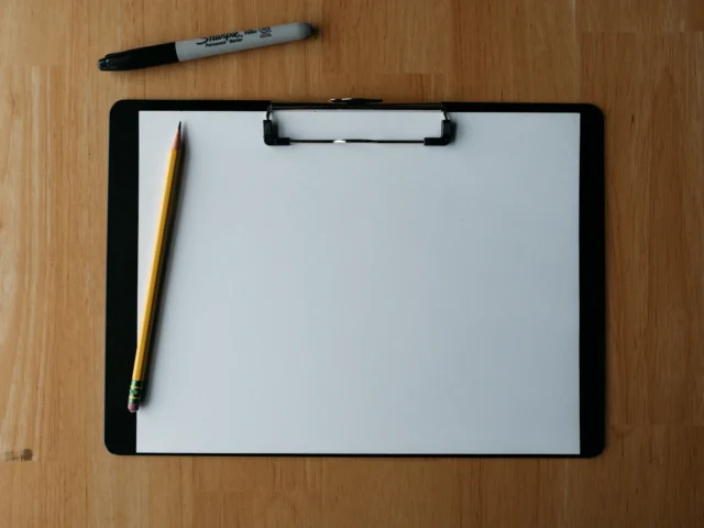 Clipboard, pencil and pen on a wooden surface