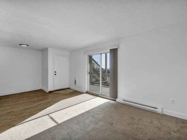 Empty room with beige carpet, wooden flooring and a sliding glass door