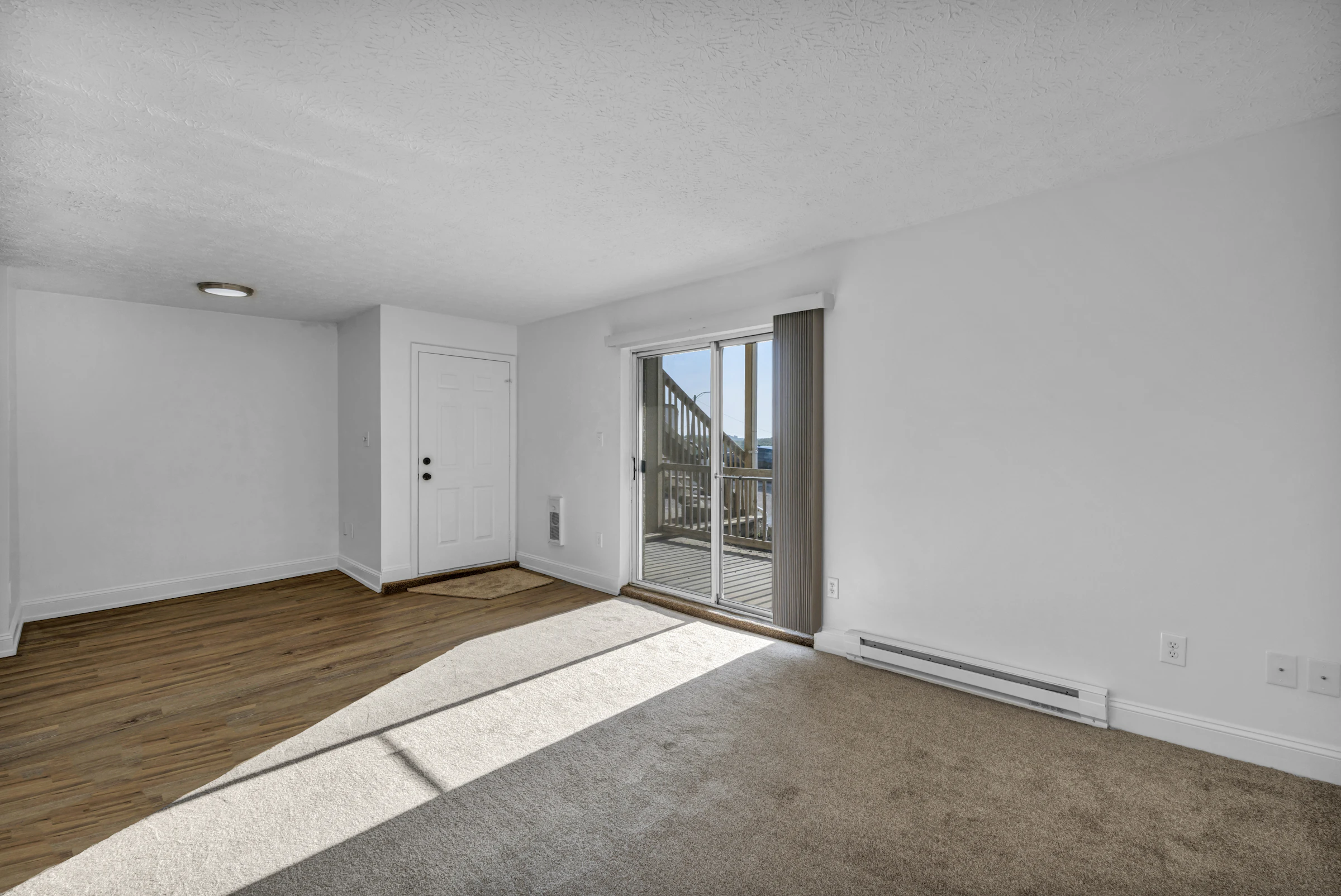 Empty room with beige carpet, wooden flooring and a sliding glass door
