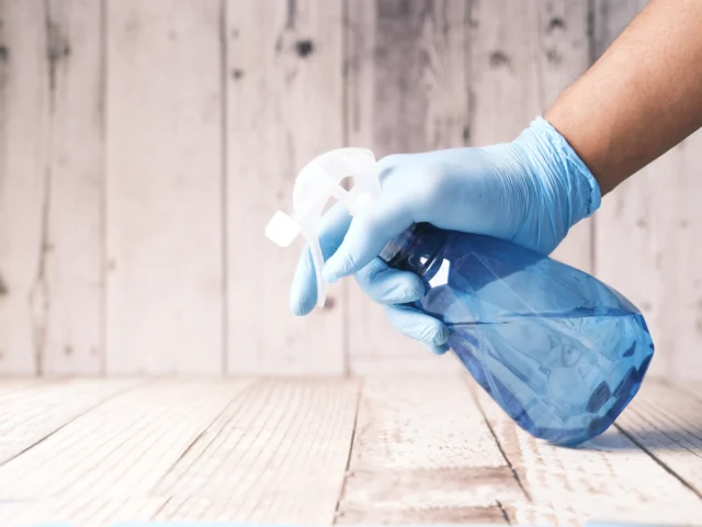 Gloved hand holding a blue spray bottle