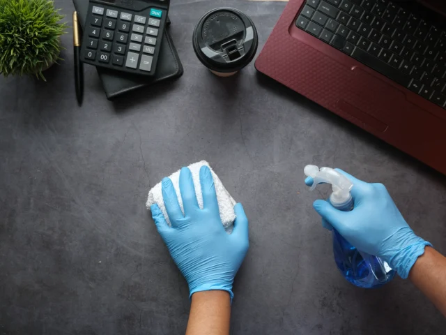 Gloved hands sanitising an office desk
