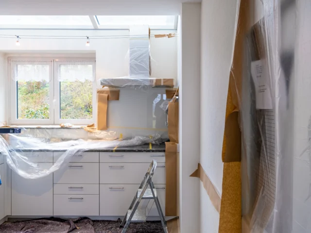 Kitchen under renovation with cabinets covered in plastic and brown paper