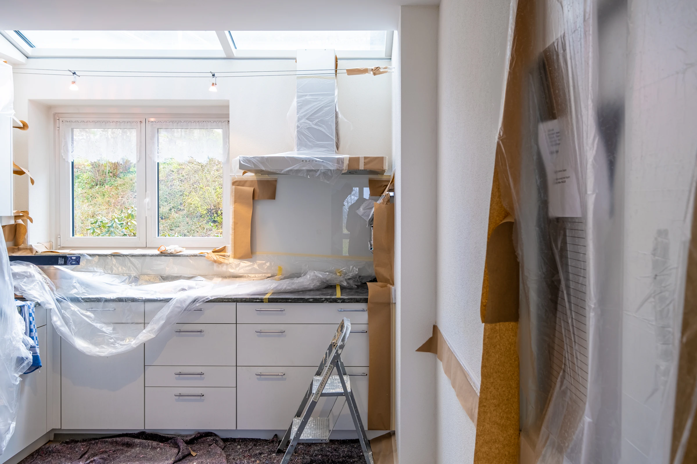 Kitchen under renovation with cabinets covered in plastic and brown paper